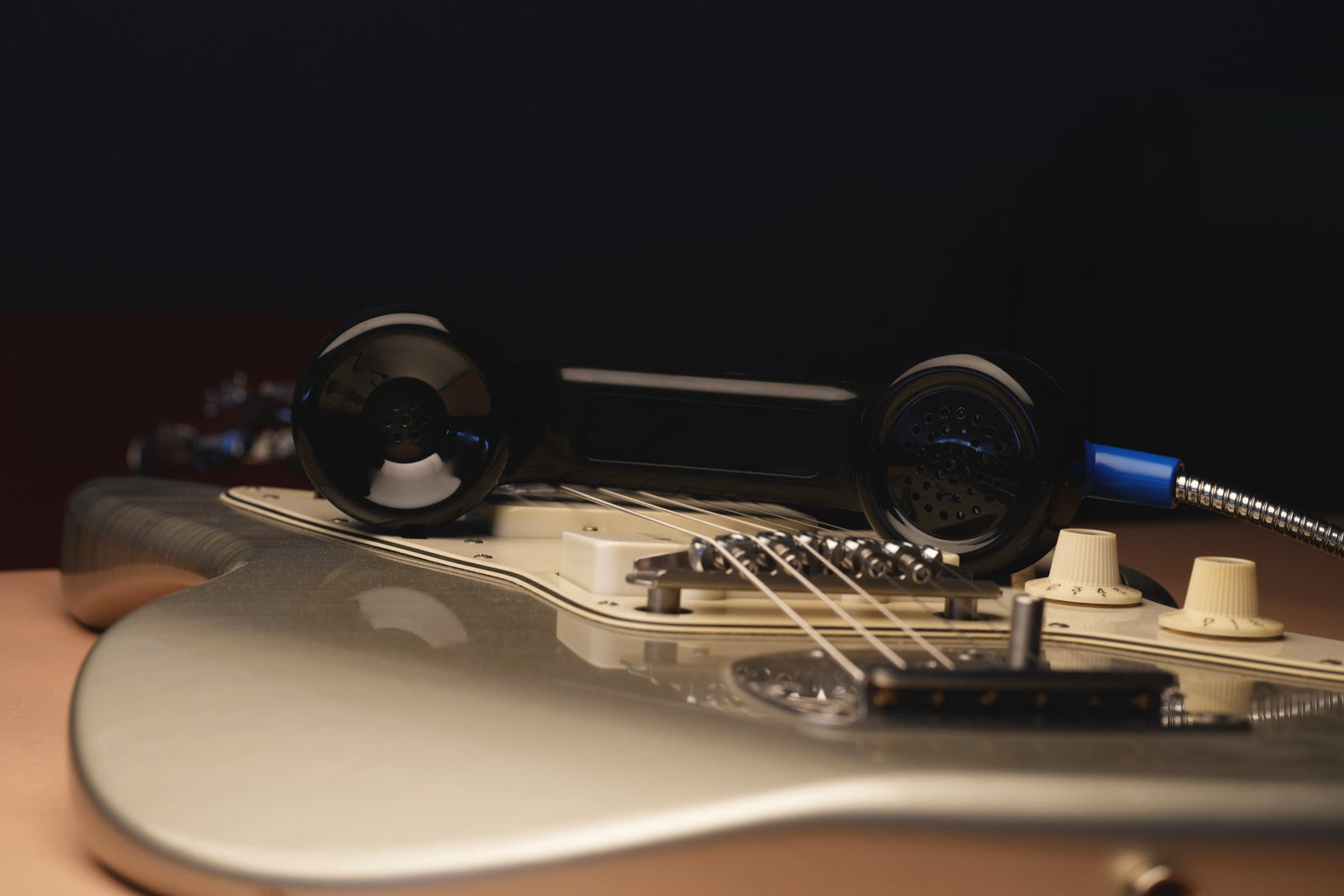 Payphone Mic negro apoyado sobre las cuerdas de una Jazzmaster, en el mismo montaje de la portada.