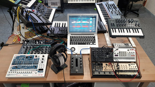 Estudio de grabación con sintetizadores y laptop mostrando DAW