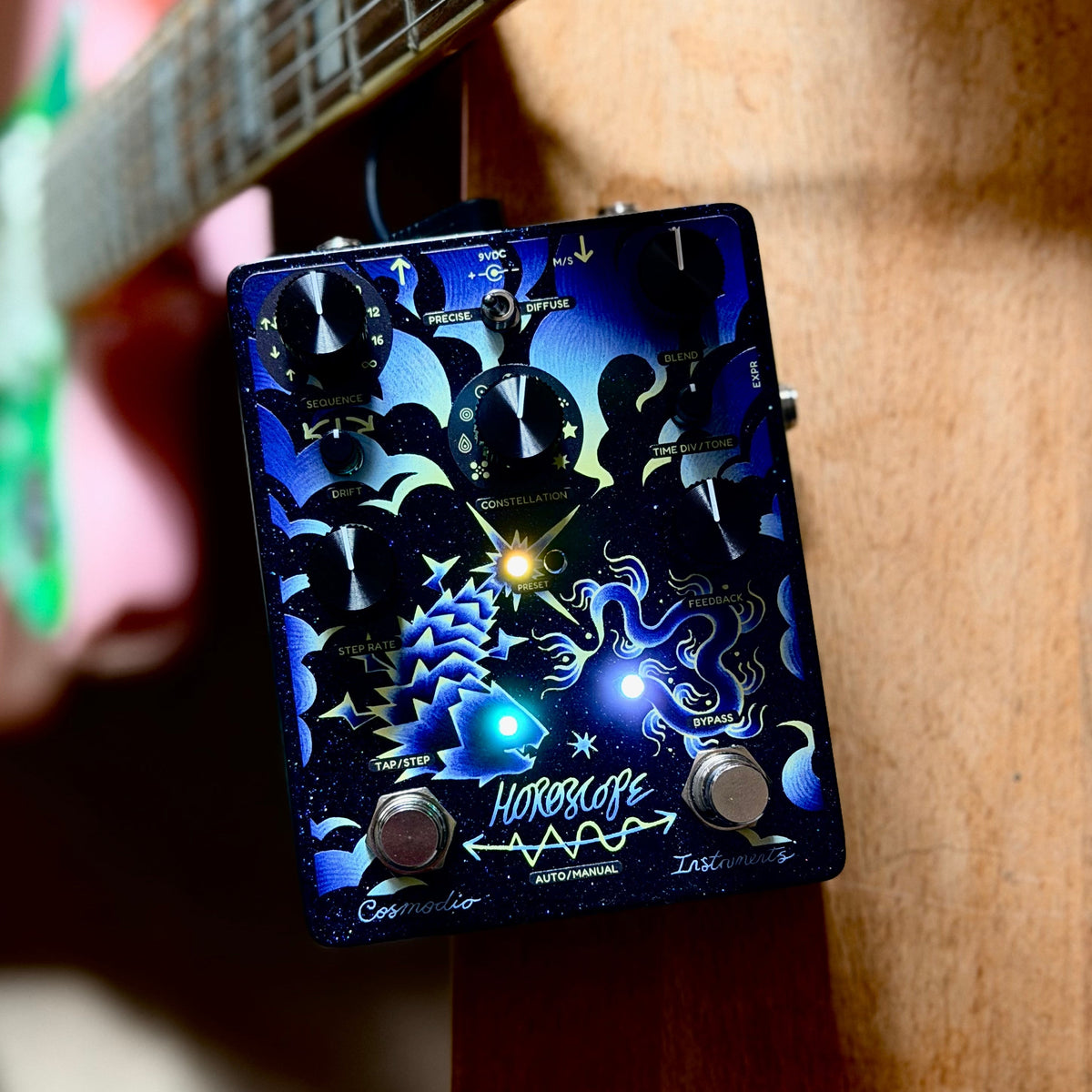 Pedal Cosmodio Horoscope junto a una guitarra, con sus indicadores iluminados