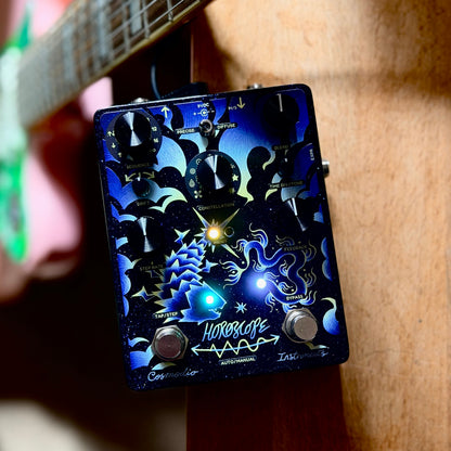 Pedal Cosmodio Horoscope junto a una guitarra, con sus indicadores iluminados