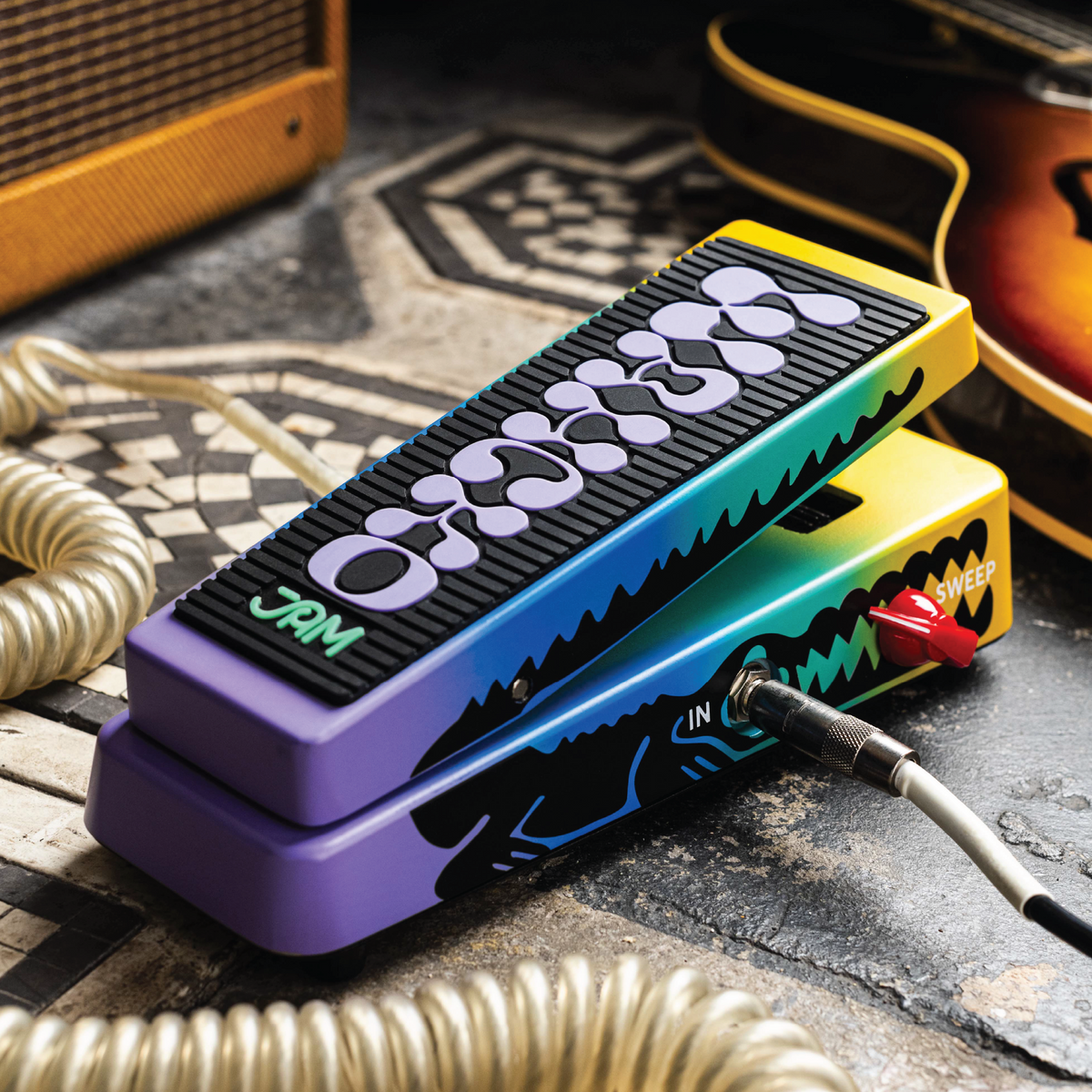 Pedal wah JAM Pedals Wahcko mk.2 en el piso con cables conectados, con guitarra y amplificador al fondo