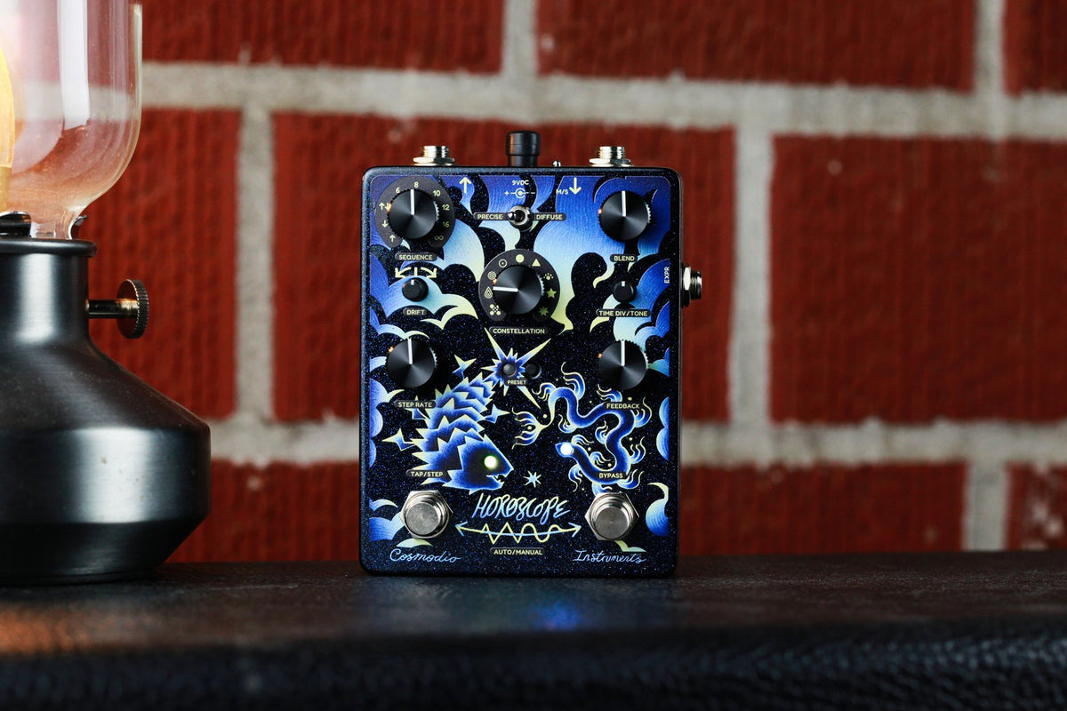 Pedal Cosmodio Horoscope sobre un amplificador, frente a una pared de ladrillos y una lámpara encendida