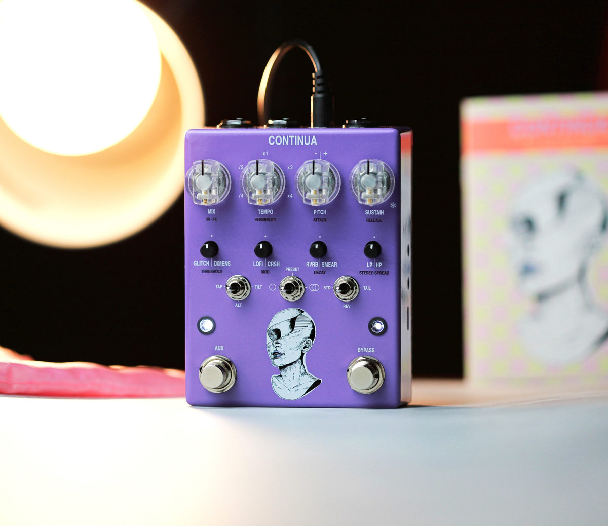 Pedal AC Noises Continua, lila con la ilustración de un busto, junto a una lámpara encendida y una lámina ilustrada