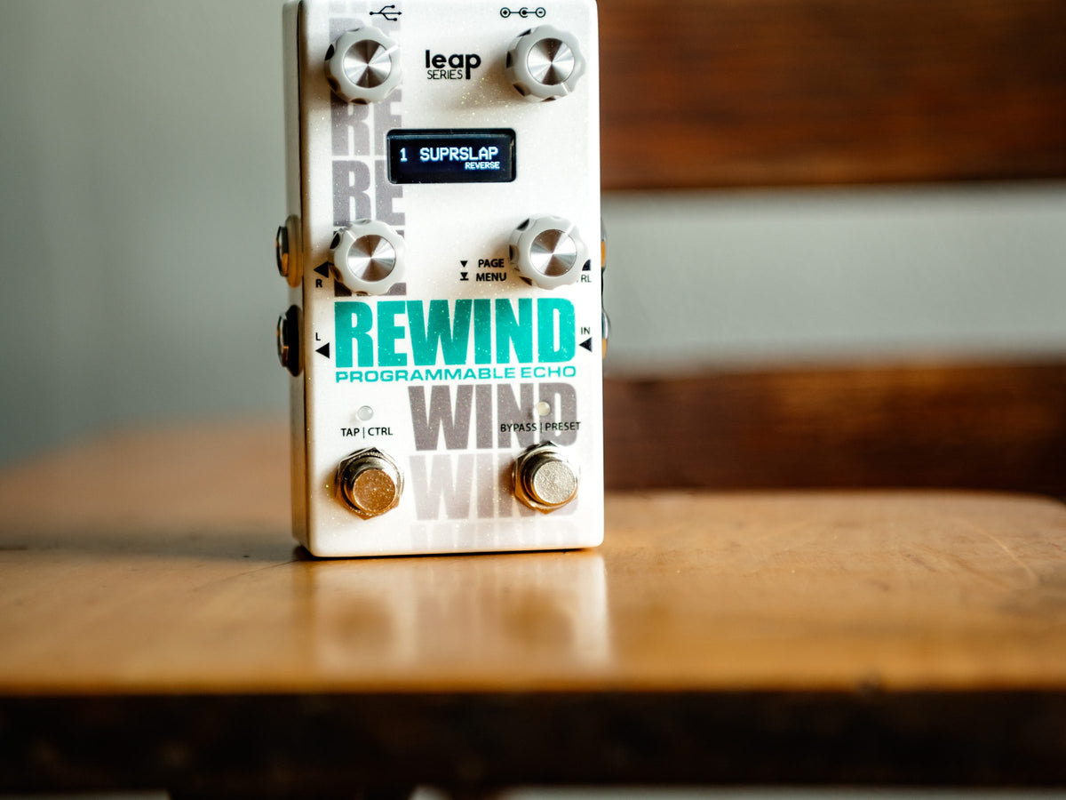 Pedal Alexander Rewind, blanco con letras verde azulado, sobre una mesa de madera