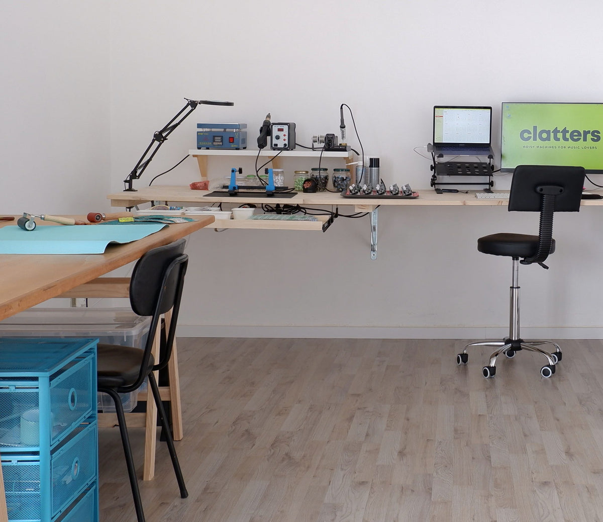 Taller de Clatters Machines: mesa de trabajo con estación de soldadura, notebook y una pantalla con el logo de la marca