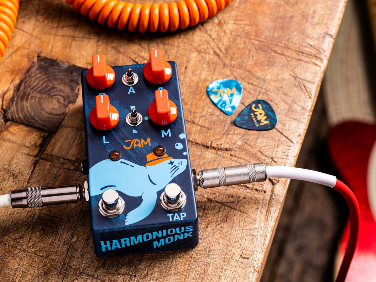 Pedal JAM Harmonious Monk mk.2, azul con perillas naranjas, sobre una mesa de madera con uñetas