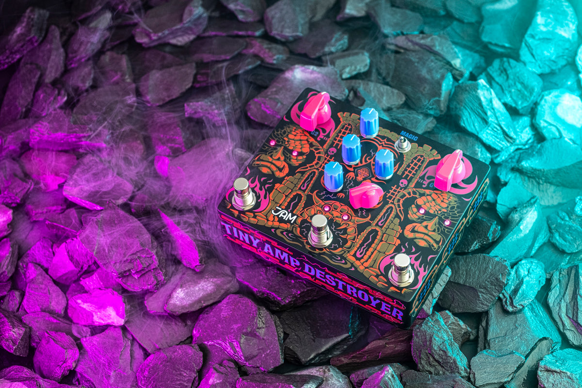JAM Pedals Tiny Amp Destroyer sobre piedras iluminadas en púrpura y cian