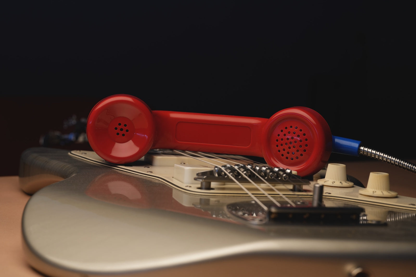 Payphone Mic rojo apoyado sobre una guitarra Jazzmaster, iluminado en penumbra.